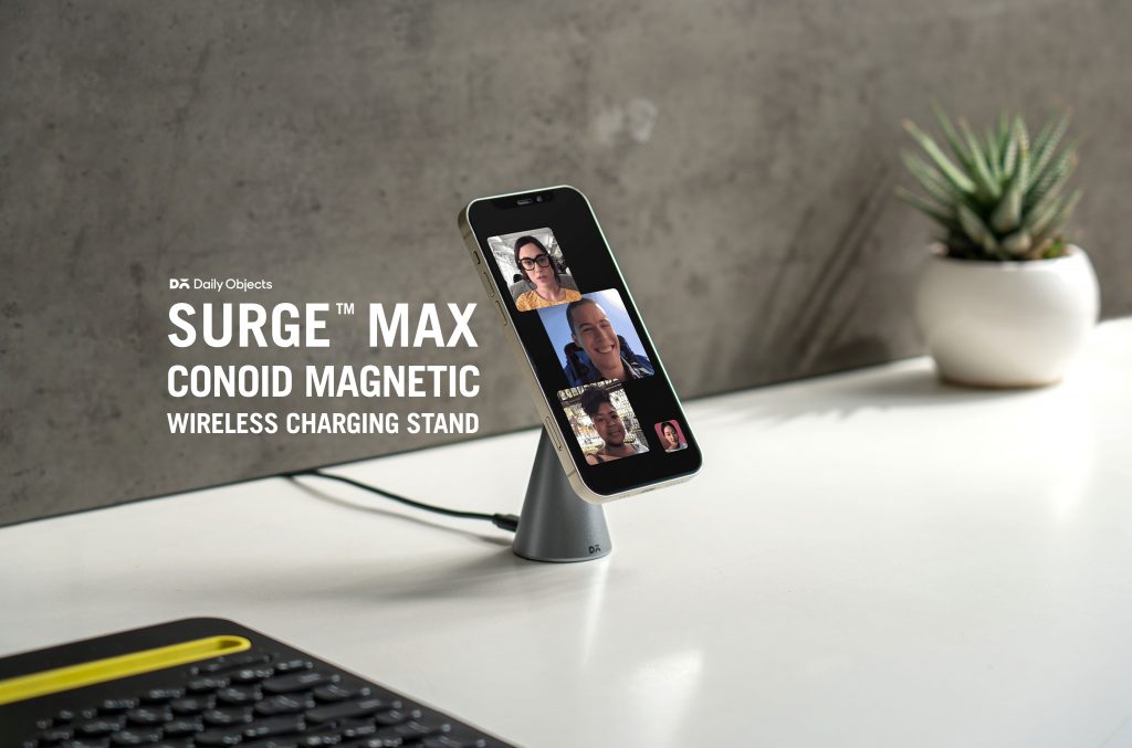DailyObjects Surge™ Conoid Universal Magnetic Charging Stand holding a smartphone upright in a sleek, modern desk setup with warm lighting and clean accessories.